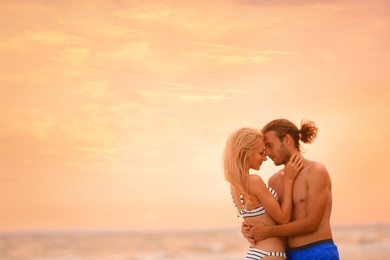 Photo of Young woman in bikini kissing her boyfriend on beach at sunset. Lovely couple