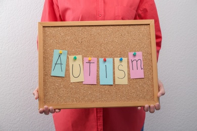 Photo of Woman holding board with word "Autism" on light background