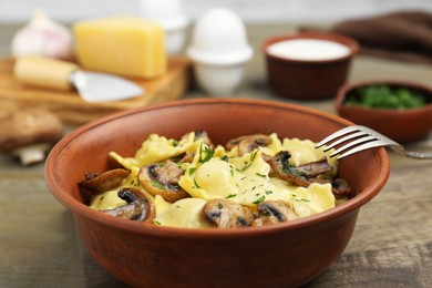 Photo of Delicious ravioli with mushrooms and fork on wooden table, closeup