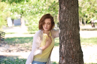 Mature woman having heart attack near tree in park