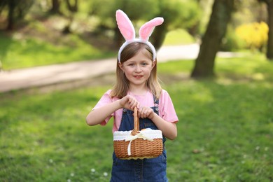 Easter celebration. Cute little girl with bunny ears holding wicker basket outdoors