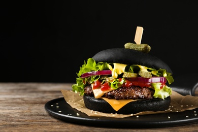 Photo of Slate plate with black burger on table. Space for text