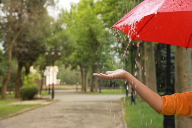Photo of Young woman with umbrella under rain in park, closeup. Space for text