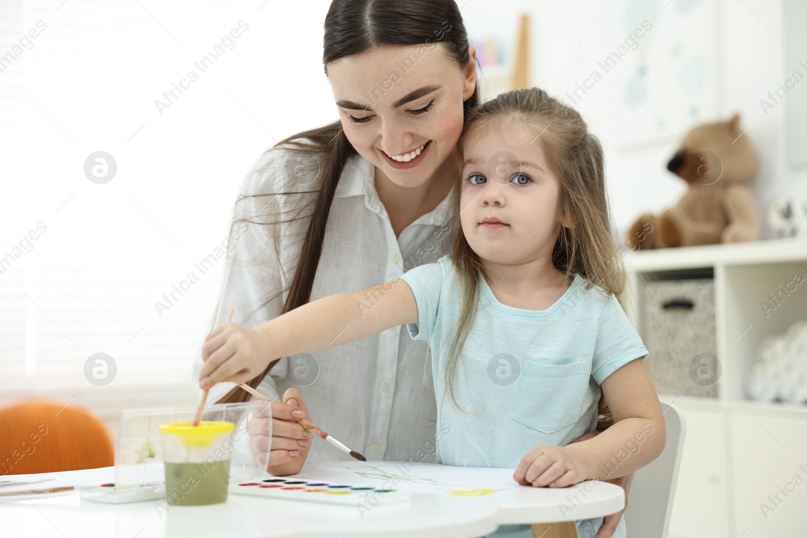 Photo of Mother and her little daughter painting with watercolor at home