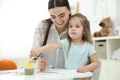 Mother and her little daughter painting with watercolor at home