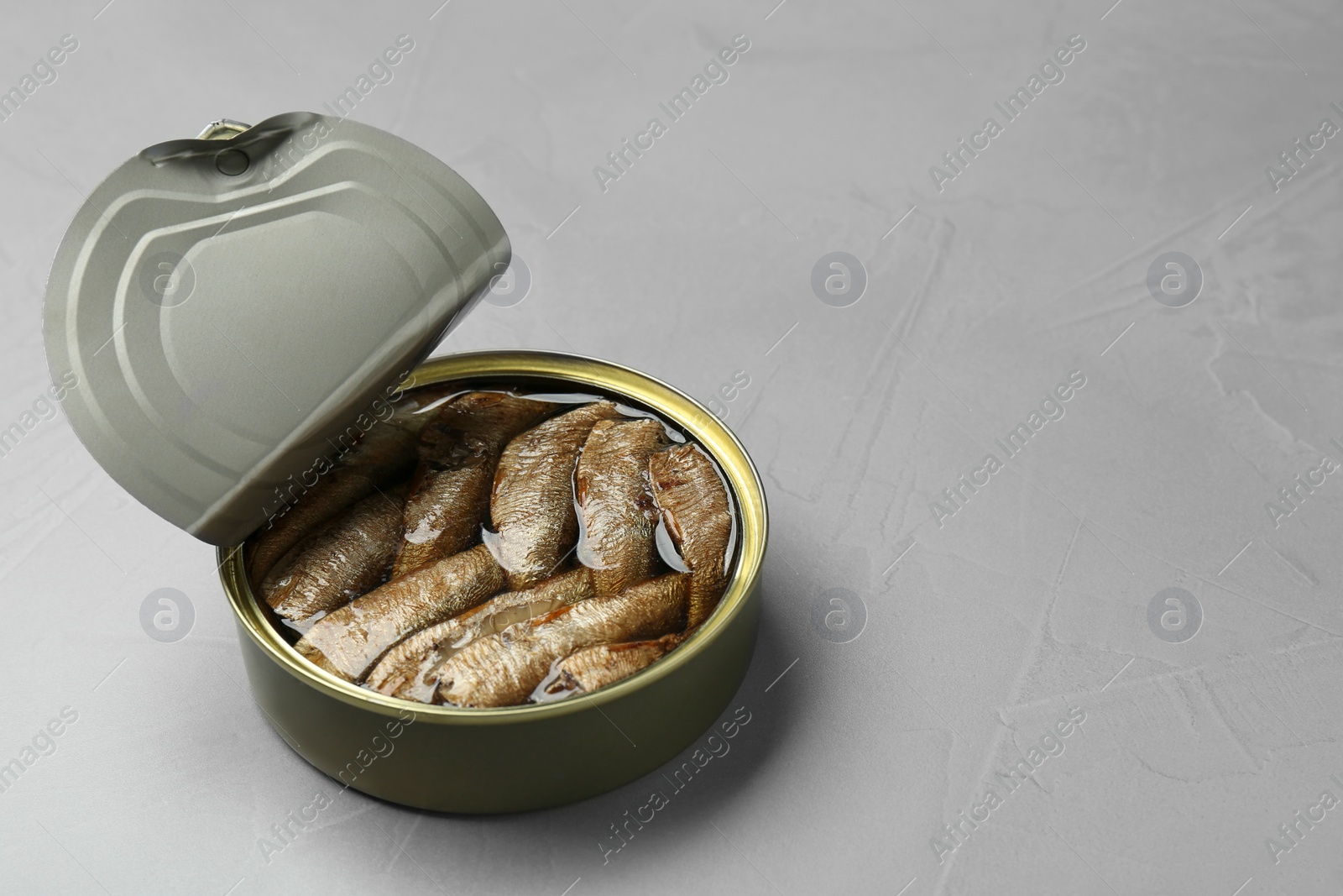 Photo of Open tin can of sprats on light grey table. Space for text