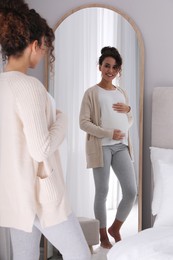 Photo of Pregnant young African-American woman near mirror at home