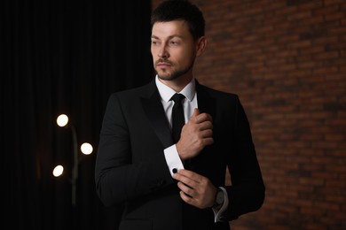 Photo of Man wearing stylish suit and cufflinks near brick wall