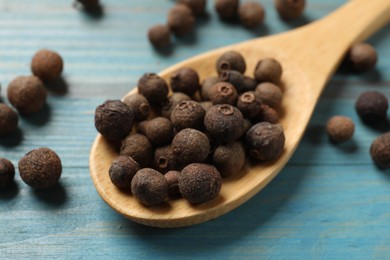 Photo of Aromatic allspice pepper grains and spoon on light blue wooden table, closeup