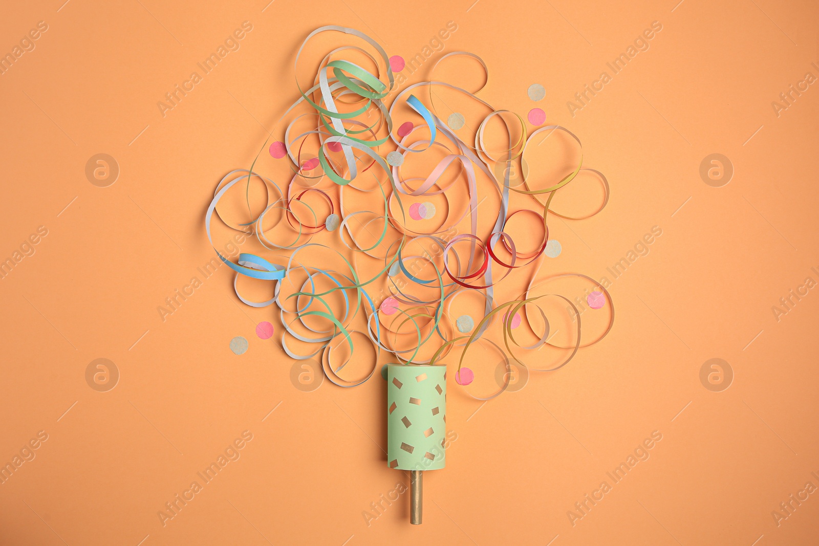 Photo of Beautiful serpentine and confetti bursting out of party popper on coral background, flat lay