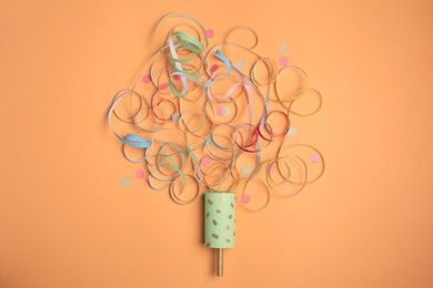 Photo of Beautiful serpentine and confetti bursting out of party popper on coral background, flat lay