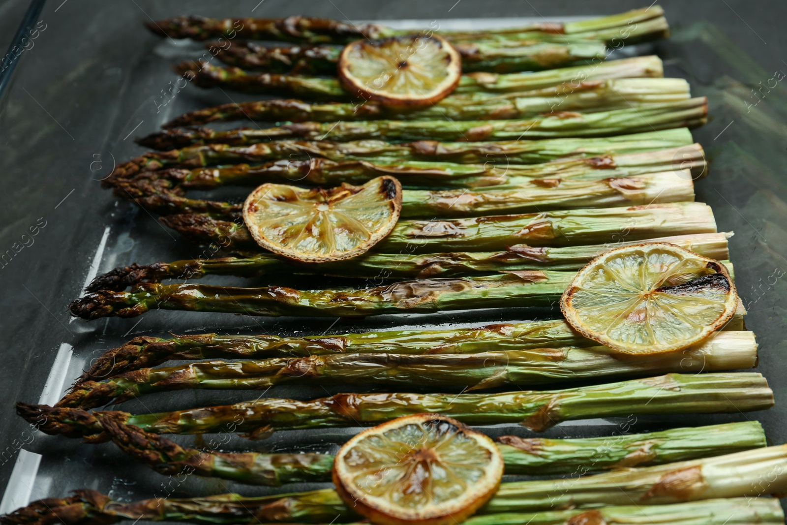 Photo of Oven baked asparagus with lemon slices in glass dish on table, closeup