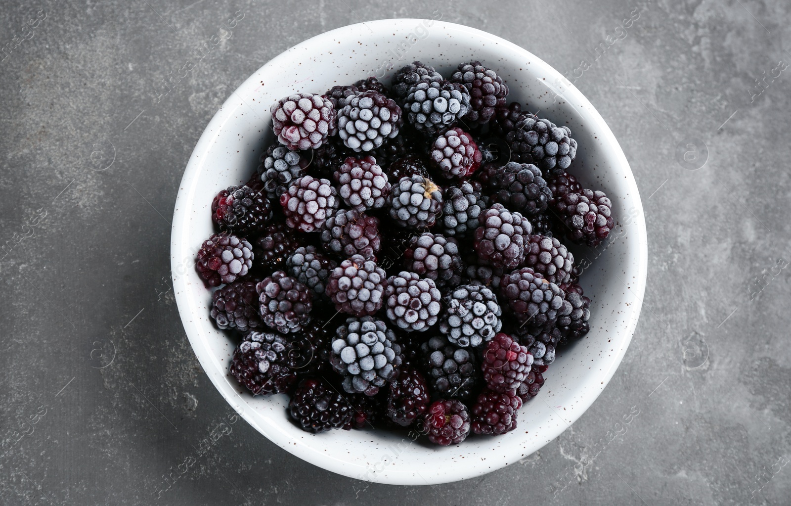 Photo of Tasty frozen blackberries in bowl on grey table, top view
