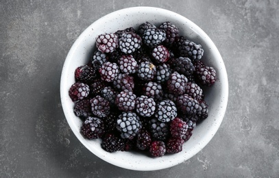 Tasty frozen blackberries in bowl on grey table, top view