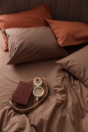 Cup of hot coffee and books on bed with stylish linens, above view