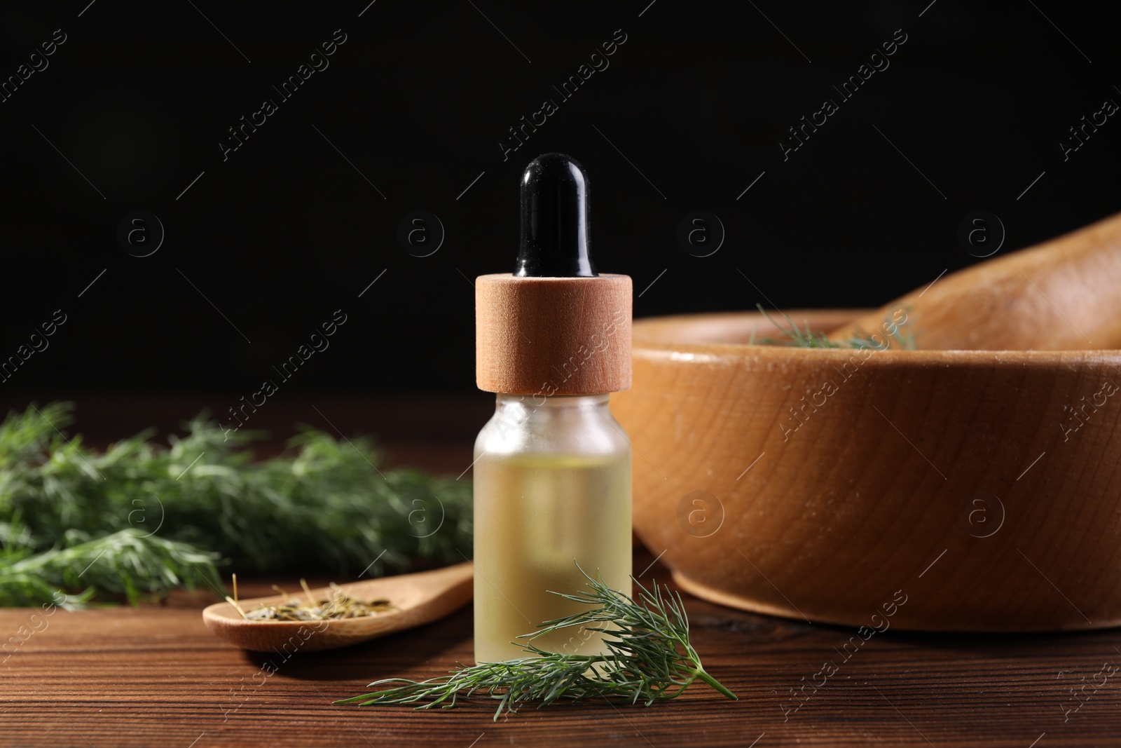 Photo of Bottle of essential oil and fresh dill on wooden table