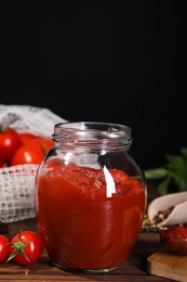 Photo of Jar of tasty tomato paste and ingredients on wooden table, space for text