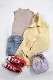 Pair of stylish red sneakers, clothes and bag on white fabric, flat lay