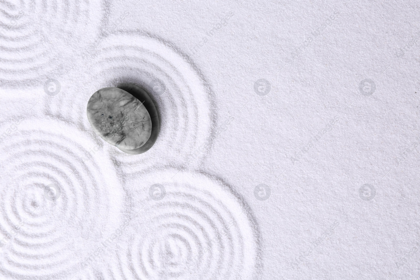 Photo of Zen garden stones on white sand with pattern, top view. Space for text