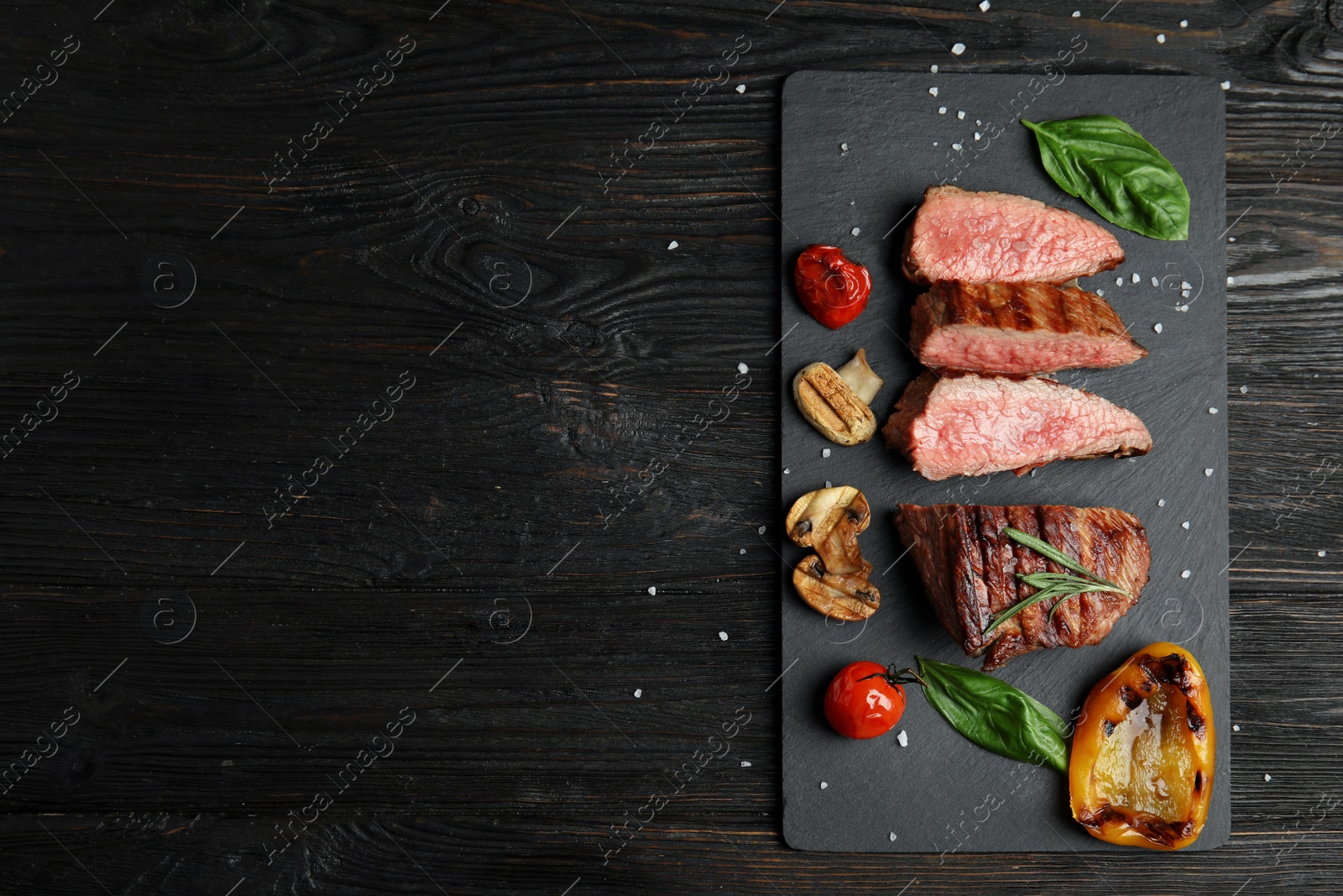 Photo of Board with slices of grilled meat on black wooden table, top view. Space for text