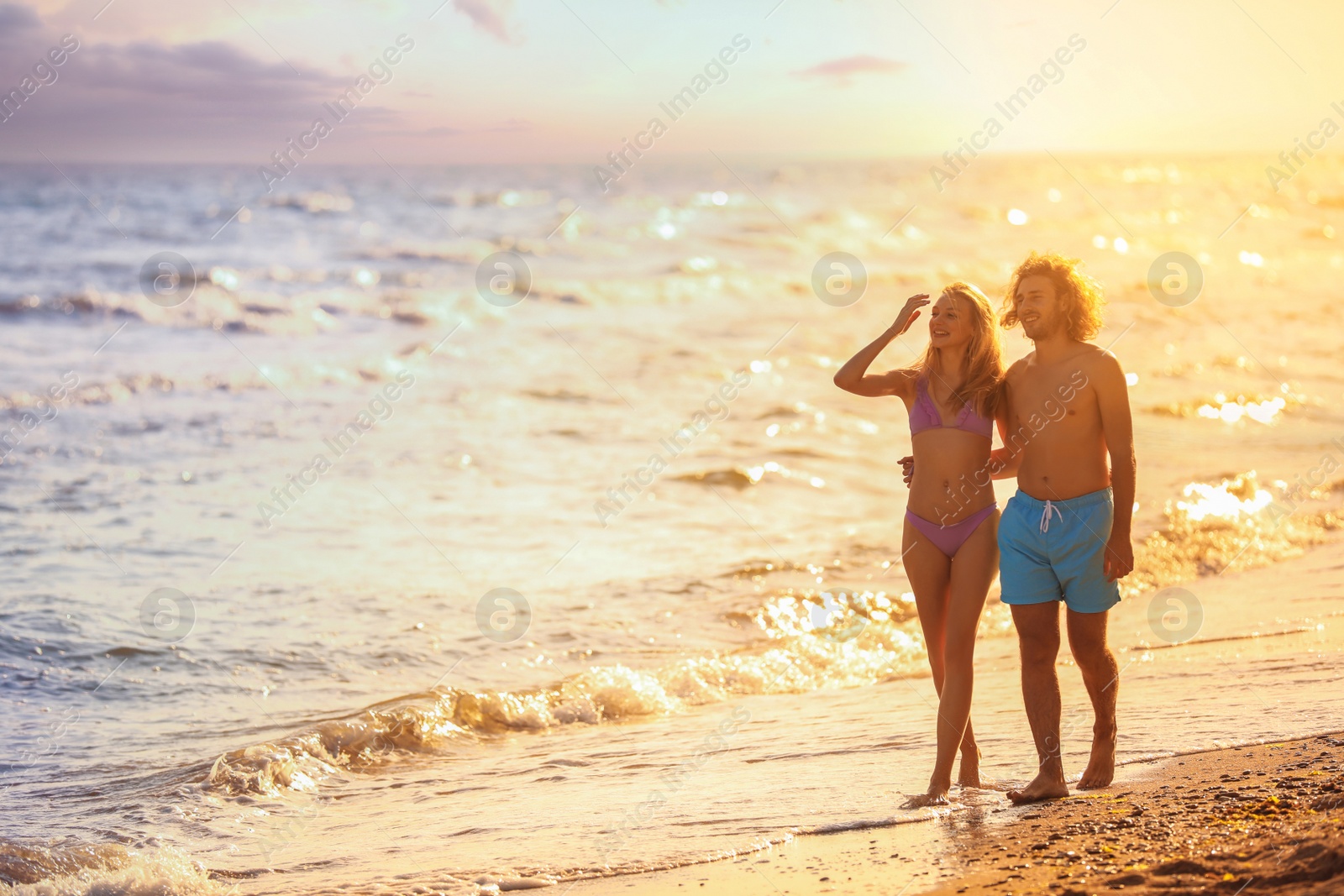 Photo of Young woman in bikini and her boyfriend on beach at sunset. Lovely couple