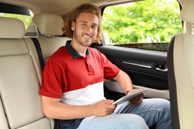 Attractive young man with tablet on backseat in luxury car