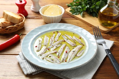 Photo of Tasty pickled anchovies with spices on wooden table