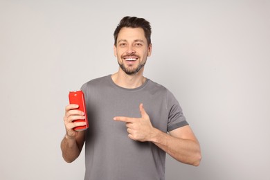 Happy man holding red tin can with beverage on light grey background