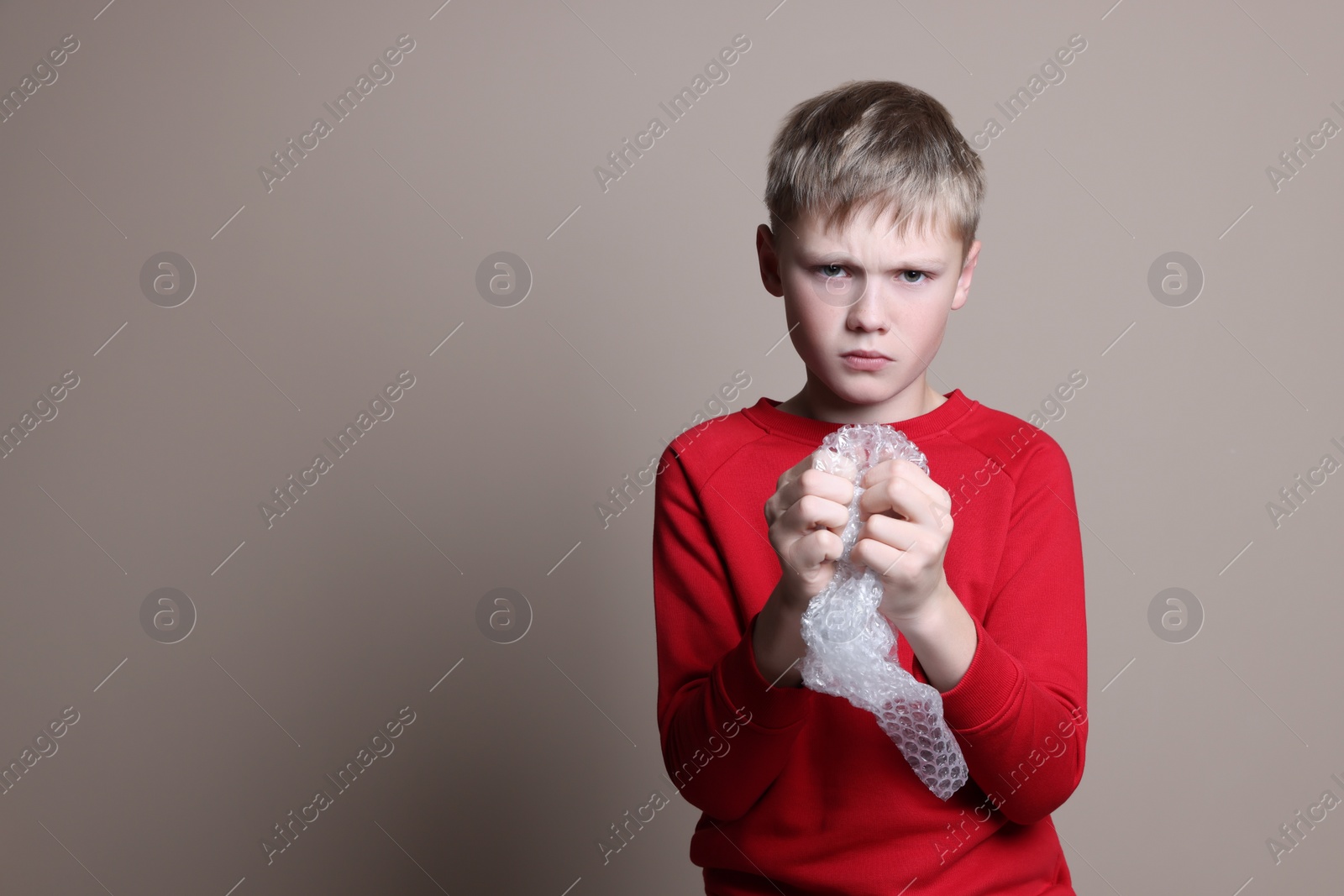 Photo of Sad boy popping bubble wrap on beige background, space for text. Stress relief