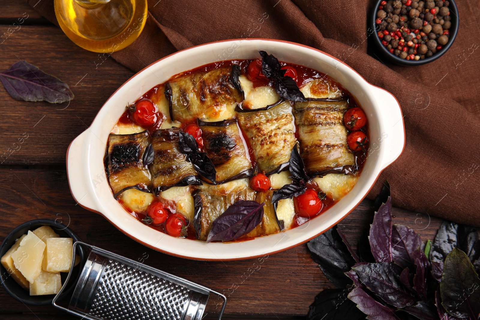 Photo of Tasty eggplant rolls with tomatoes and cheese in baking dish on wooden table, flat lay
