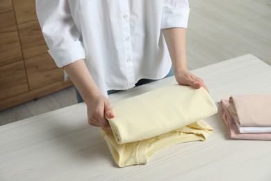 Woman folding clothes at white wooden table indoors, closeup