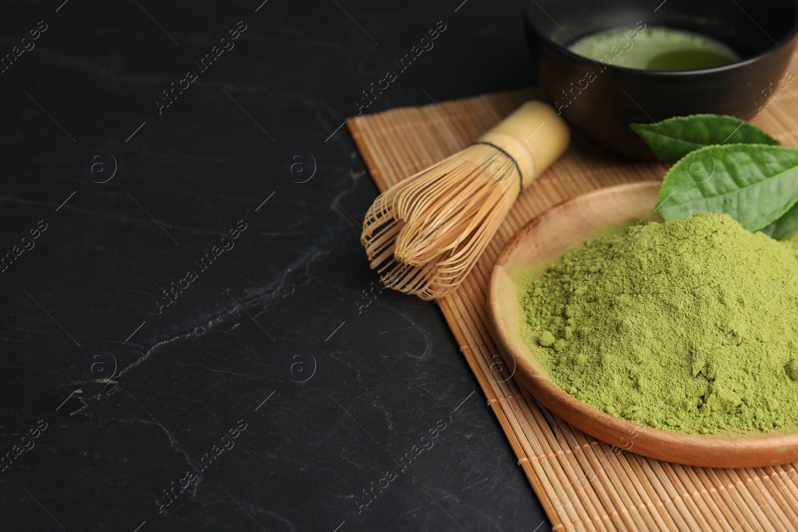 Photo of Green matcha powder and bamboo whisk on black table, closeup. Space for text