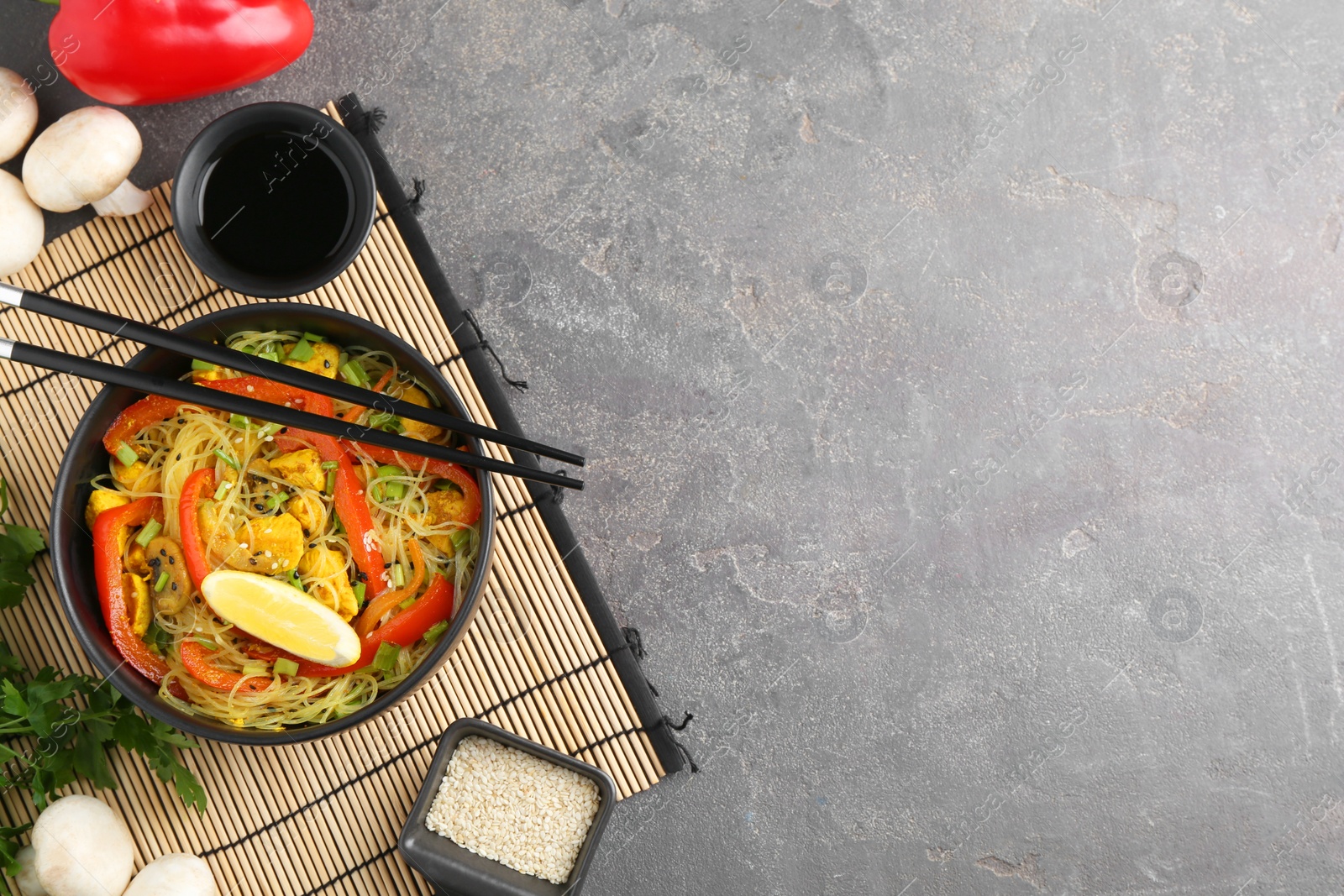 Photo of Stir-fry. Delicious cooked noodles with chicken and vegetables in bowl served on gray textured table, flat lay. Space for text