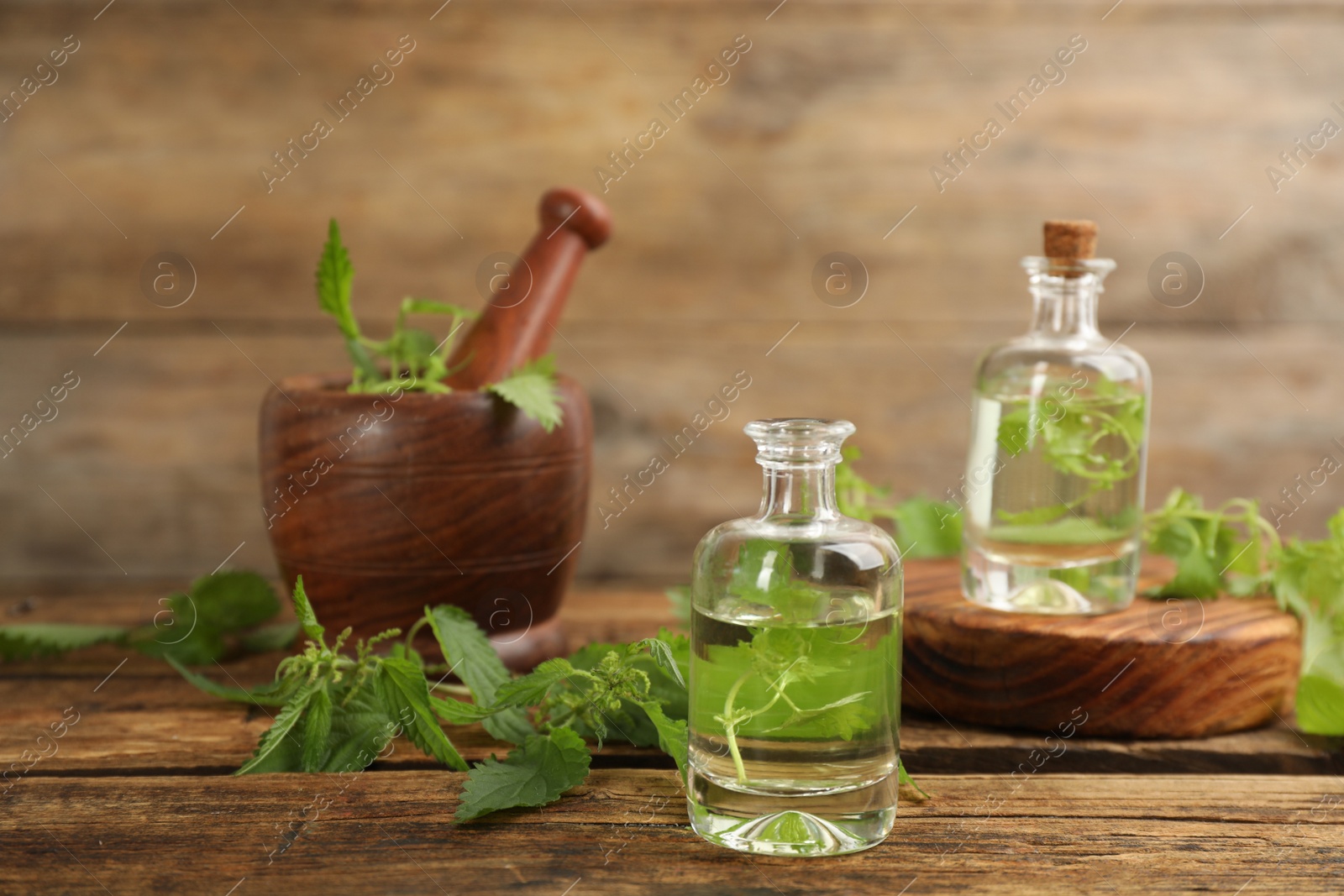 Photo of Stinging nettle extract and leaves on wooden background. Natural hair care