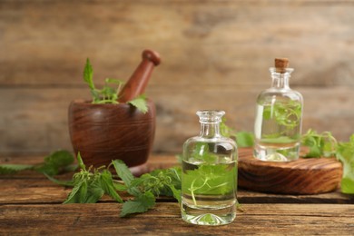 Photo of Stinging nettle extract and leaves on wooden background. Natural hair care