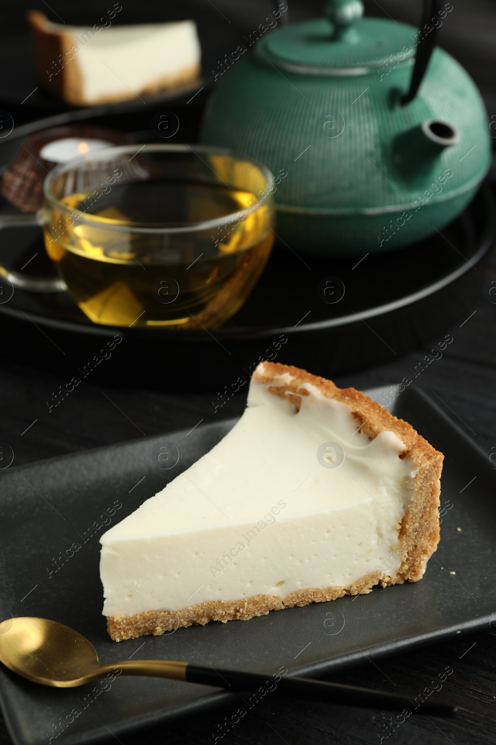 Photo of Piece of tasty vegan tofu cheesecake and spoon on black wooden table, space for text