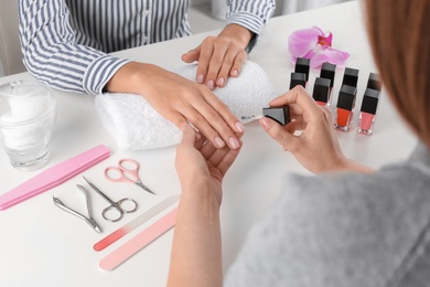 Photo of Manicurist painting client's nails with polish in salon, closeup