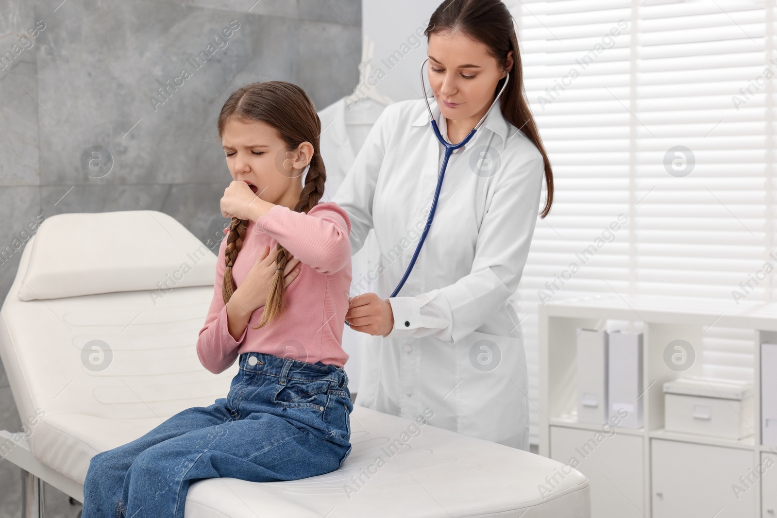 Photo of Doctor examining coughing girl in hospital. Cold symptoms