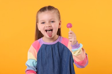 Photo of Little girl with lollipop showing tongue on orange background