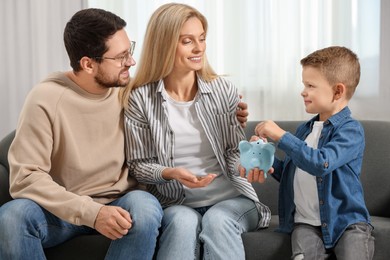 Photo of Family budget. Little boy putting coin into piggy bank and his parents at home