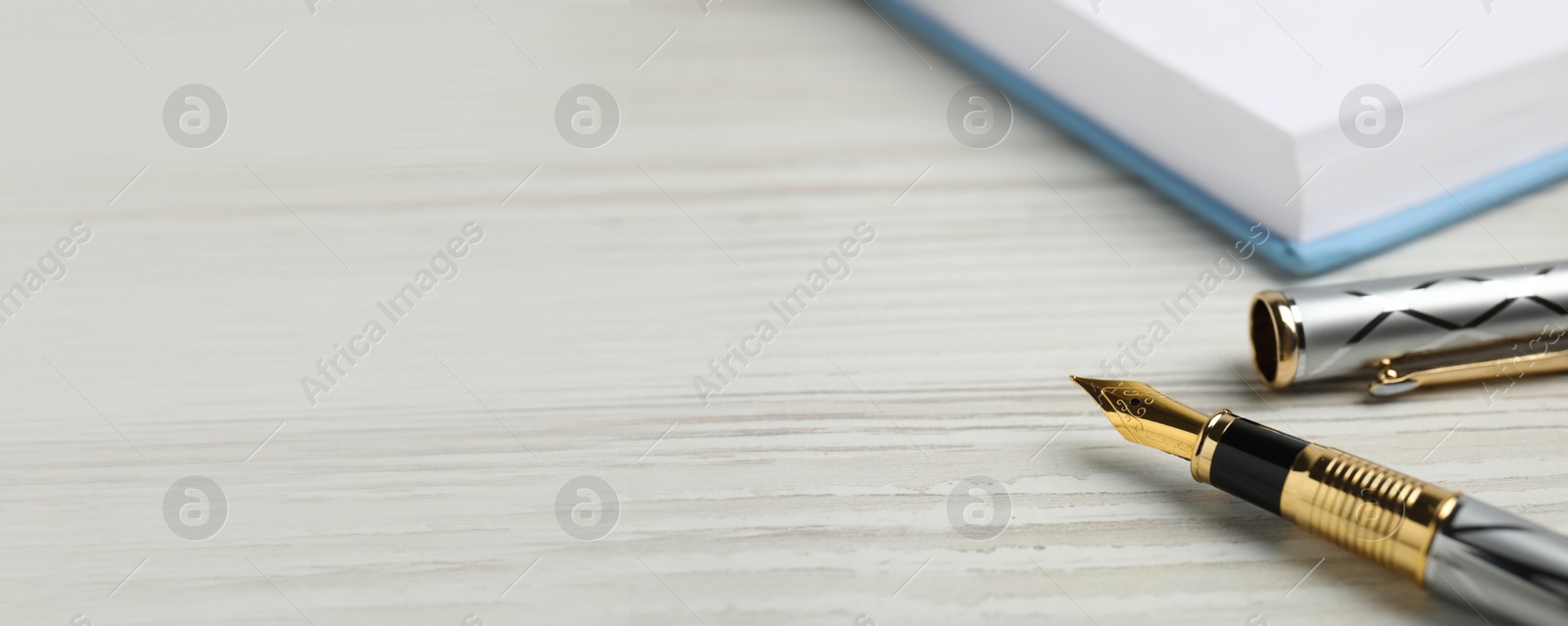 Image of Beautiful fountain pen with ornate nib on white wooden table, closeup view with space for text. Banner design