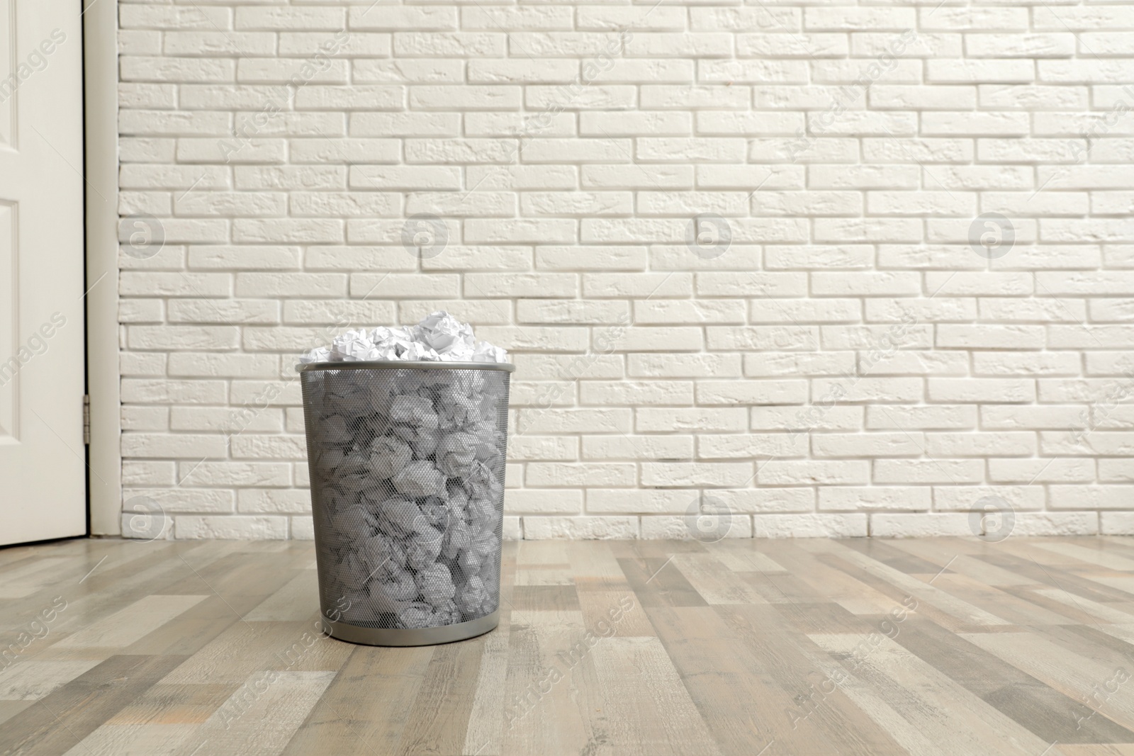 Photo of Metal bin with crumpled paper on floor against brick wall, space for text