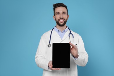 Photo of Doctor with stethoscope holding blank tablet on light blue background, space for design. Cardiology concept