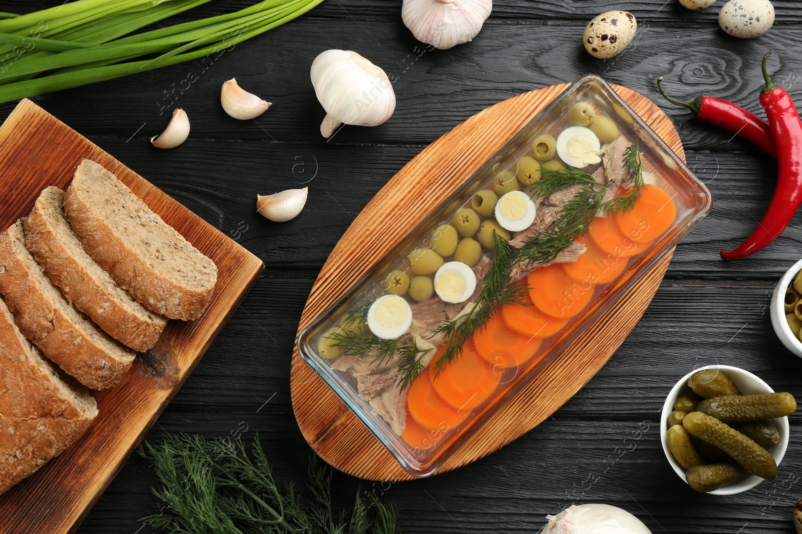 Photo of Delicious aspic with meat and ingredients on black wooden table, flat lay