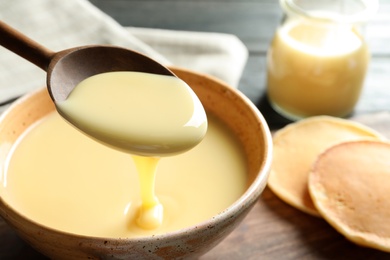 Spoon of pouring condensed milk over bowl on table, closeup with space for text. Dairy products