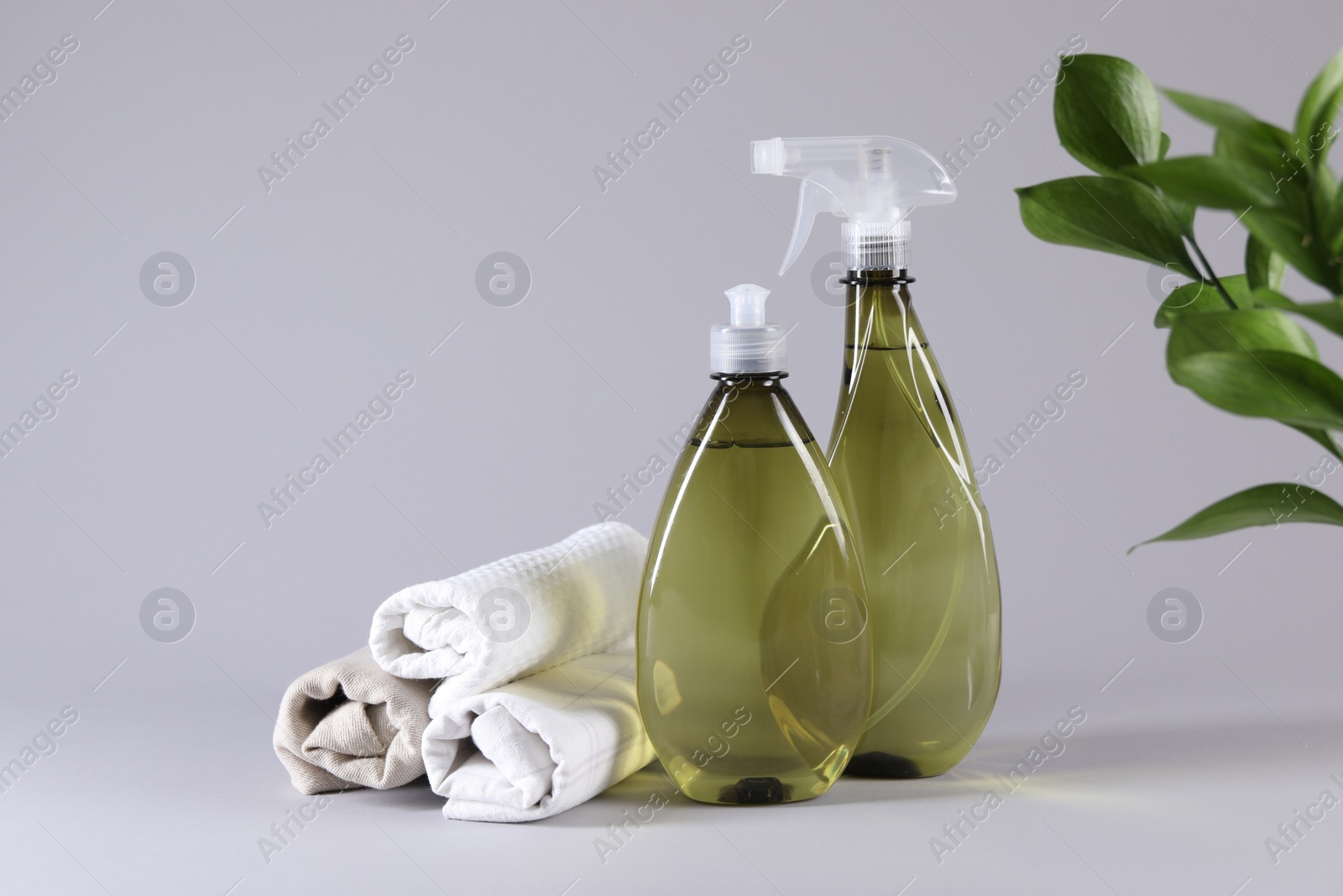 Photo of Bottles of cleaning product and rolled rags on light background