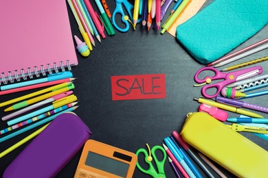 Photo of Flat lay composition with school stationery and word Sale on blackboard