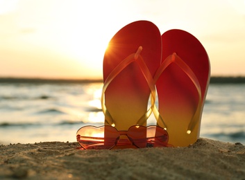 Photo of Stylish flip flops with sunglasses on sand near sea, space for text. Beach accessories