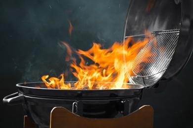 Photo of New modern barbecue grill with burning firewood on dark background