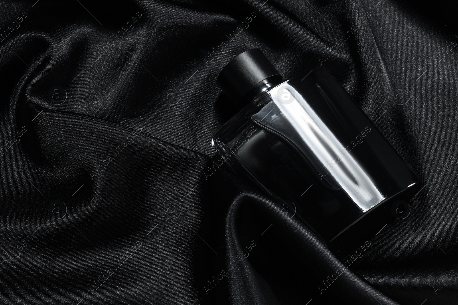 Photo of Luxury men's perfume in bottle on black satin fabric, top view. Space for text